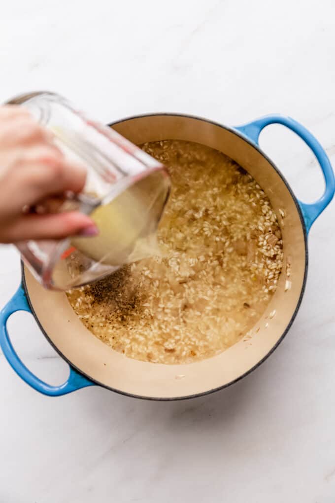 a measuring cup pouring vegetable stock into a pot of rice