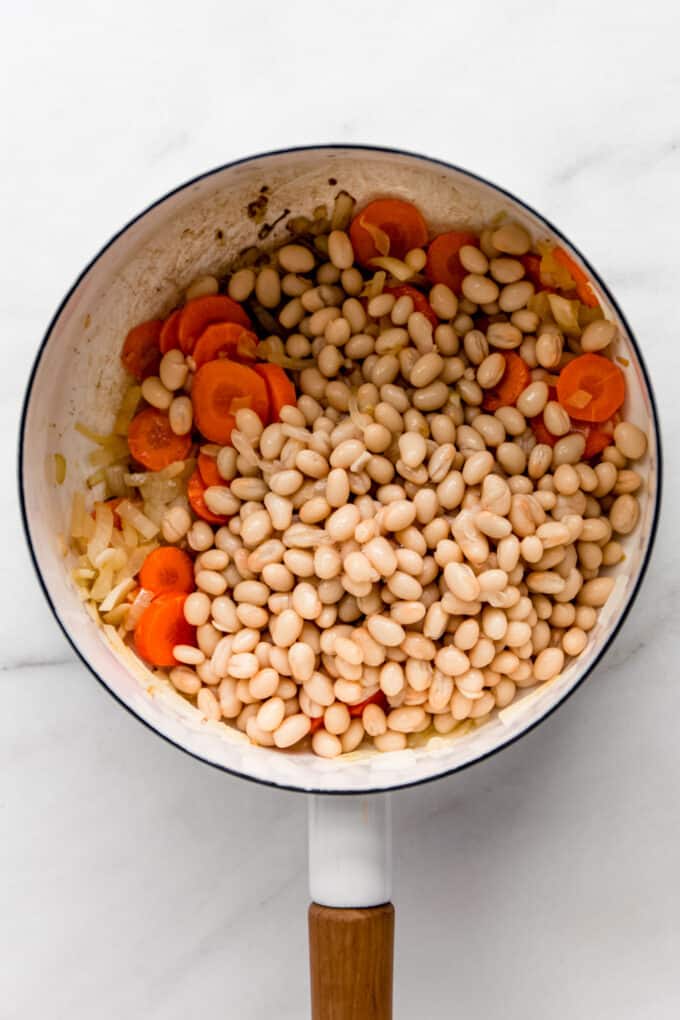 white beans, carrots and onions in a white pot