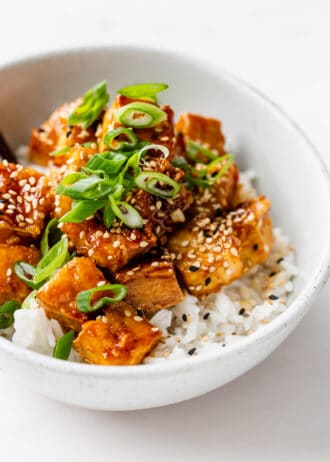 a bowl of honey garlic tofu over rice with scallions and sesame seeds
