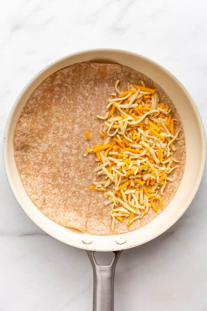 shredded cheese on a tortilla in a pan