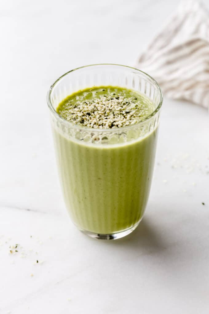 A glass of green protein smoothie with a beige napkin on the side