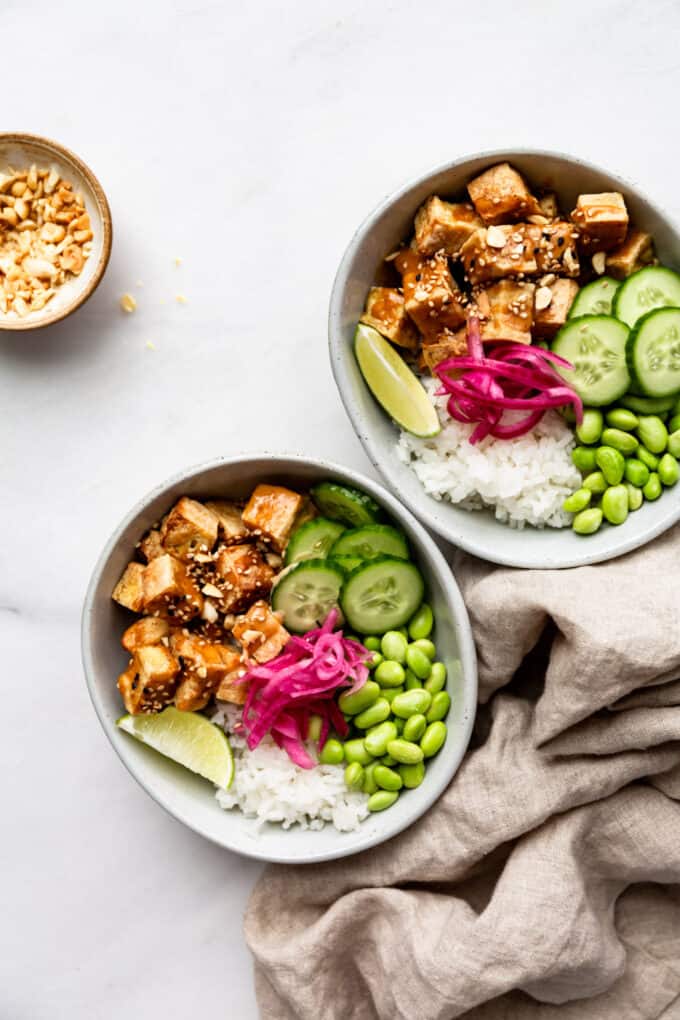 two peanut tofu bowls with a napkin and a small bowl of crushed peanuts