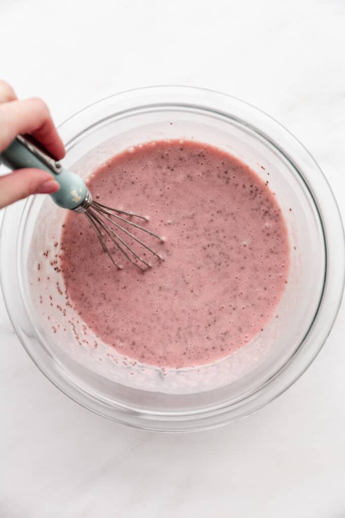 a whisk whisking strawberry milk and chia seeds in a bowl