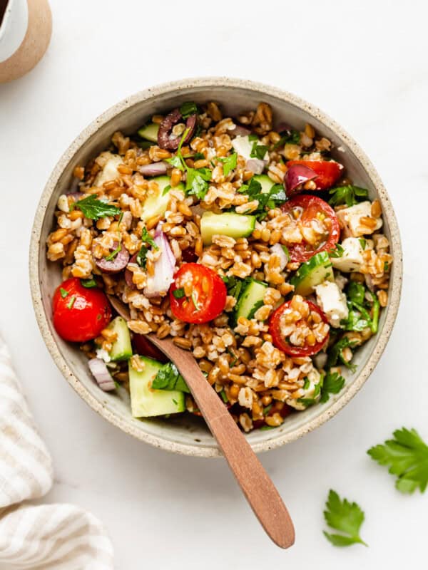 a bowl of Greek farro salad with a wood spoon in it