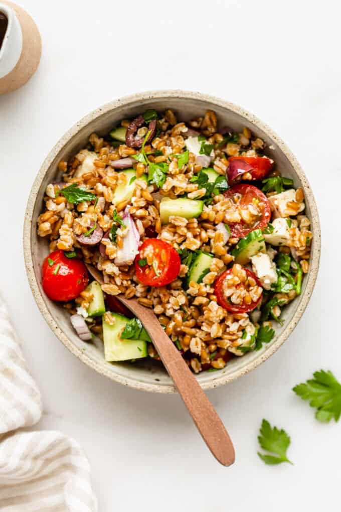 a bowl of Greek farro salad with a wood spoon in it