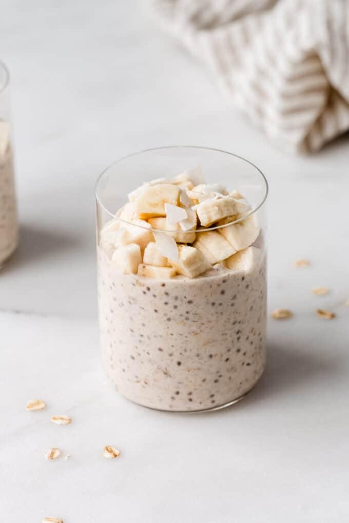 a glass of banana overnight oats topped with banana and coconut flakes