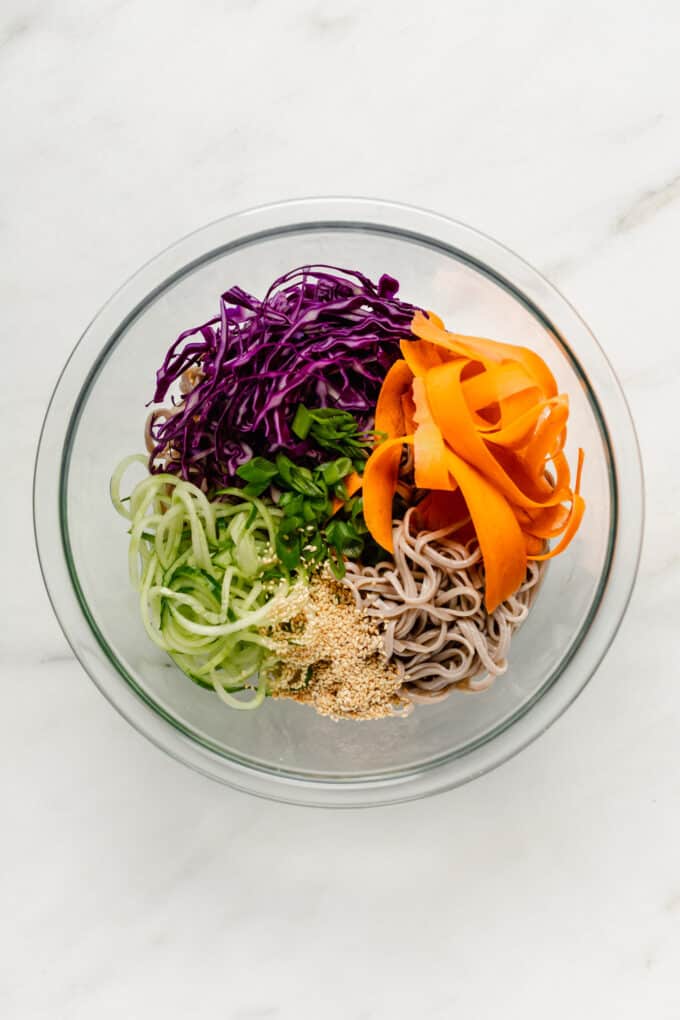 soba noodles, cabbage, carrots, cucumber, scallions and sesame seeds in a mixing bowl