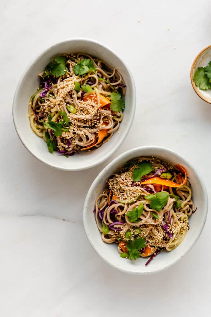 two bowls of cold soba noodle salad topped with cilantro and sesame seeds