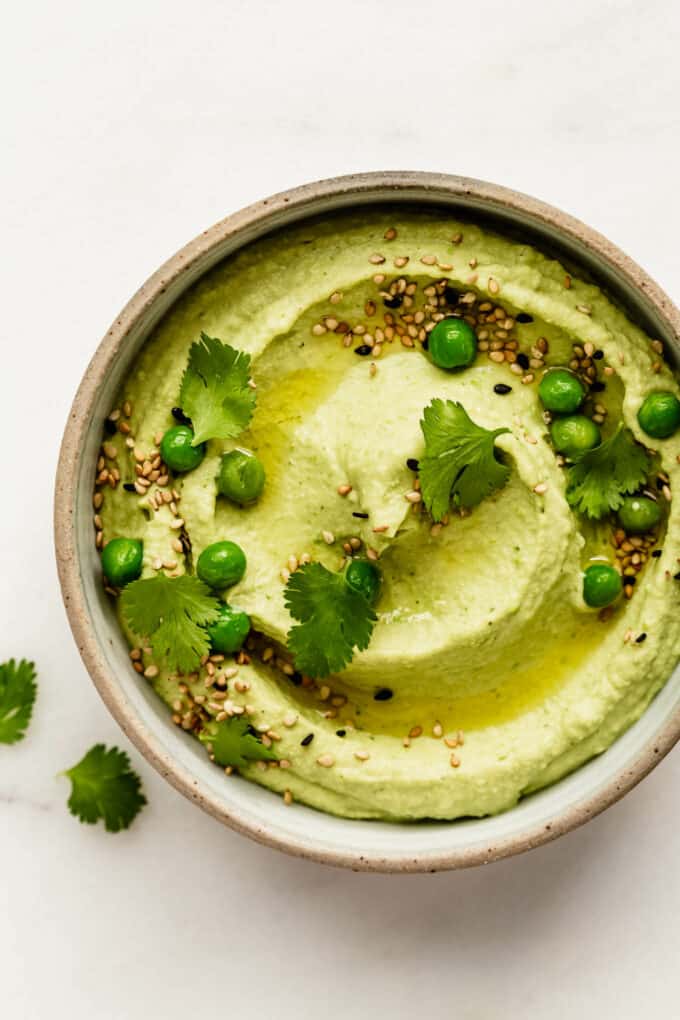 a bowl of green pea hummus topped with cilantro and peas