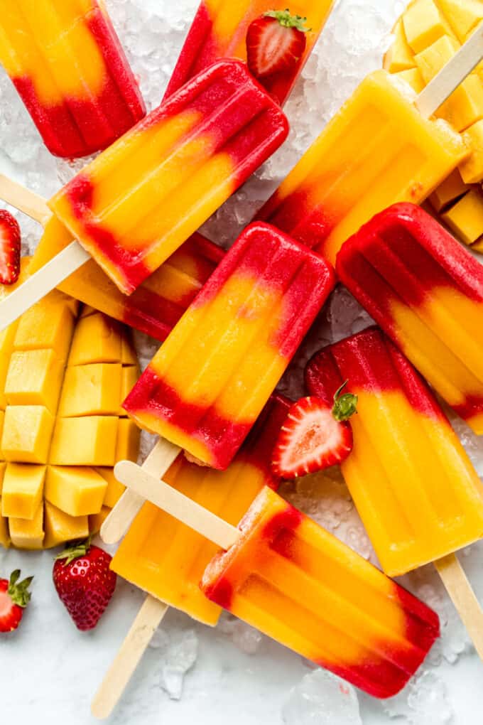 strawberry mango popsicles on ice with sliced strawberries and mango around them