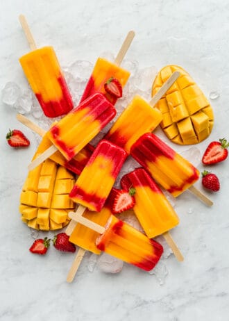 strawberry mango popsicles on a marble board with mangos and strawberries