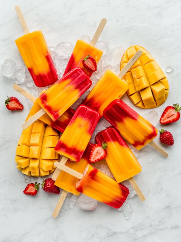 strawberry mango popsicles on a marble board with mangos and strawberries