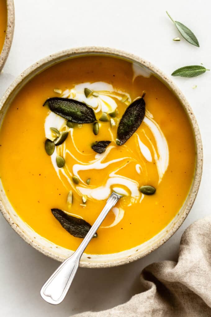 roasted acorn squash soup in a bowl with sage, pumpkin seeds and coconut milk