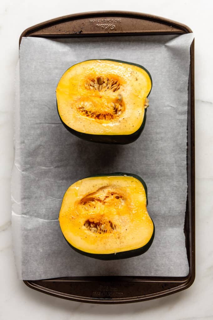 an acorn squash sliced in half on a baking tray