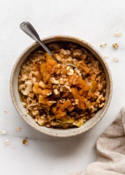 A bowl of oatmeal topped with cooked apples and walnuts