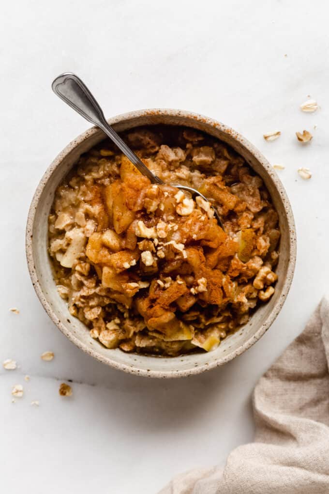 A bowl of oatmeal topped with cooked apples and walnuts