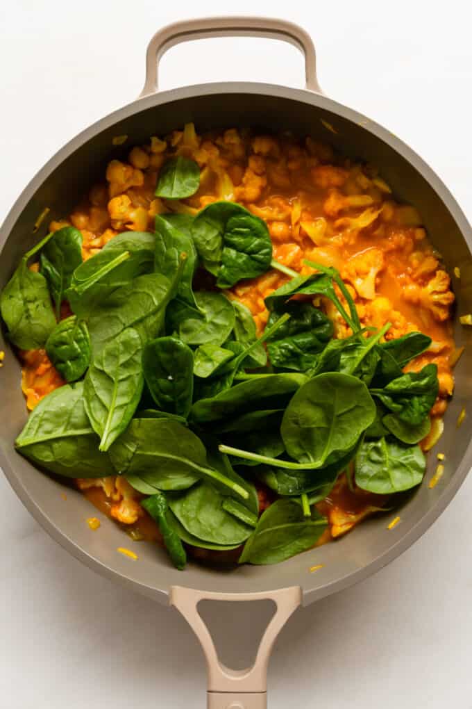 cauliflower curry and fresh spinach leaves in a pan