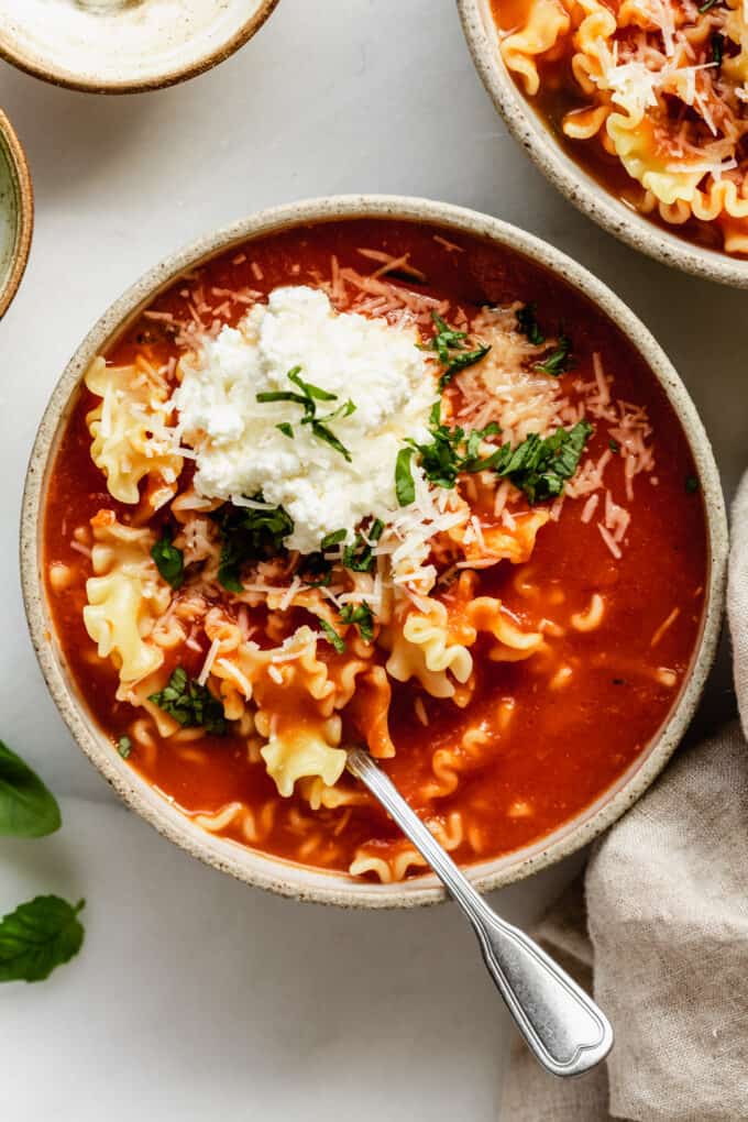 a bowl of lasagna soup topped with ricotta and basil