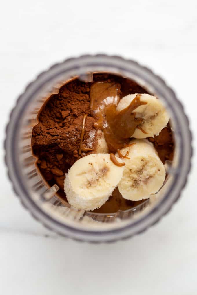 a blender with banana, almond butter and cocoa powder in it