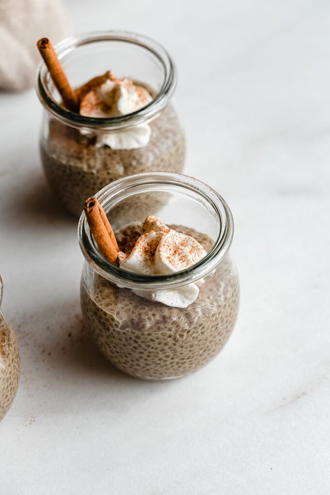 two jars of gingerbread chia pudding topped with whipped cream and cinnamon