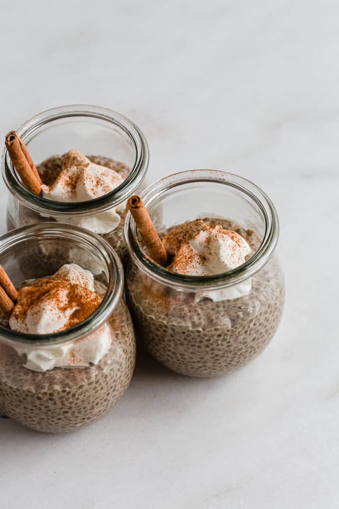 three jars of gingerbread chia pudding with whipped cream and cinnamon sticks