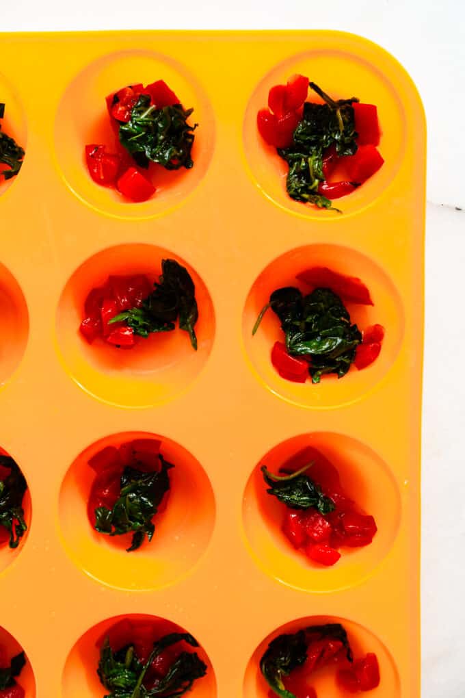 roasted red peppers and spinach in an orange muffin pan
