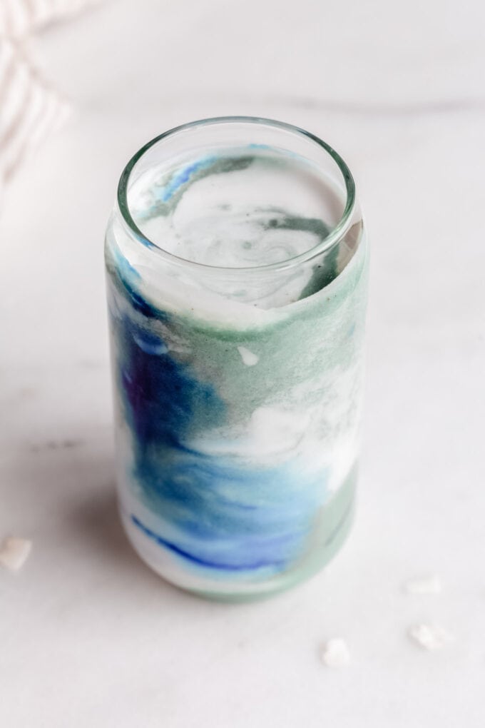 a blue spirulina smoothie in a glass topped with coconut milk
