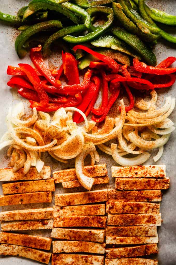 sliced tofu, onions and red and green peppers on a baking sheet