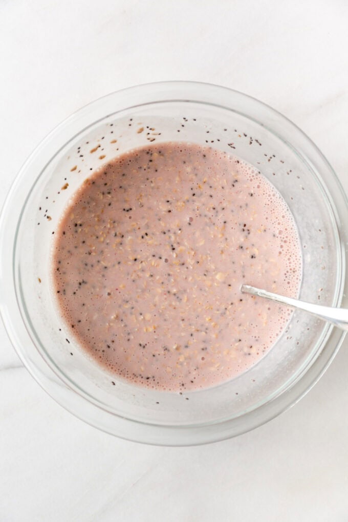 oats mixed with chia seeds and blended strawberry milk in a clear mixing bowl