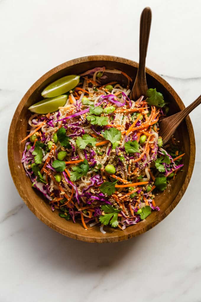 A thai noodle salad in a wooden bowl with serving spoons