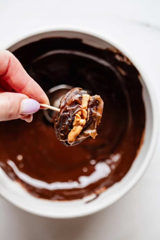 a medjool date being dipped into a bowl of dark chocoalte