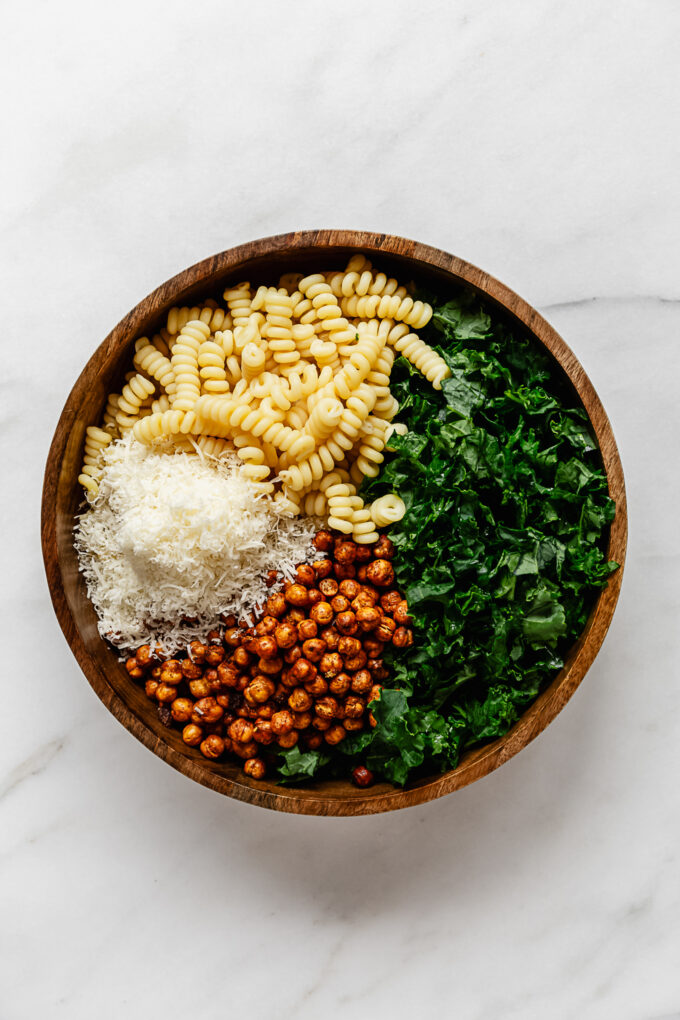 kale, pasta, roasted chickpeas and parmesan cheese in a wood serving bowl