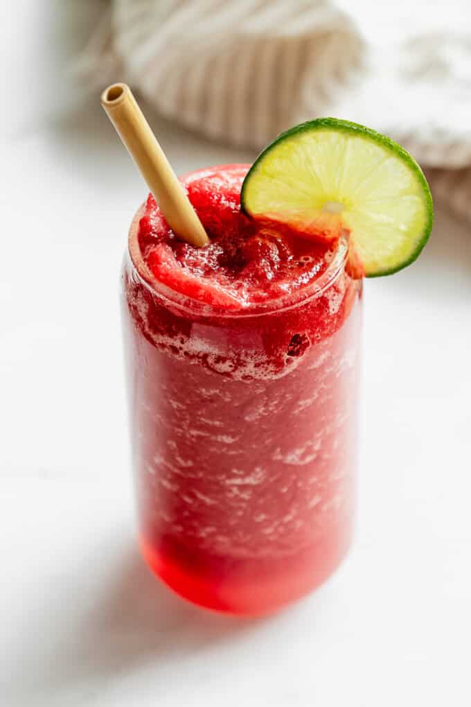 A glass of a watermelon slushie with a straw and lime slice in it