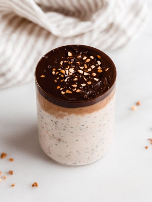 a cup of snickers overnight oats with a beige striped napkin in the back
