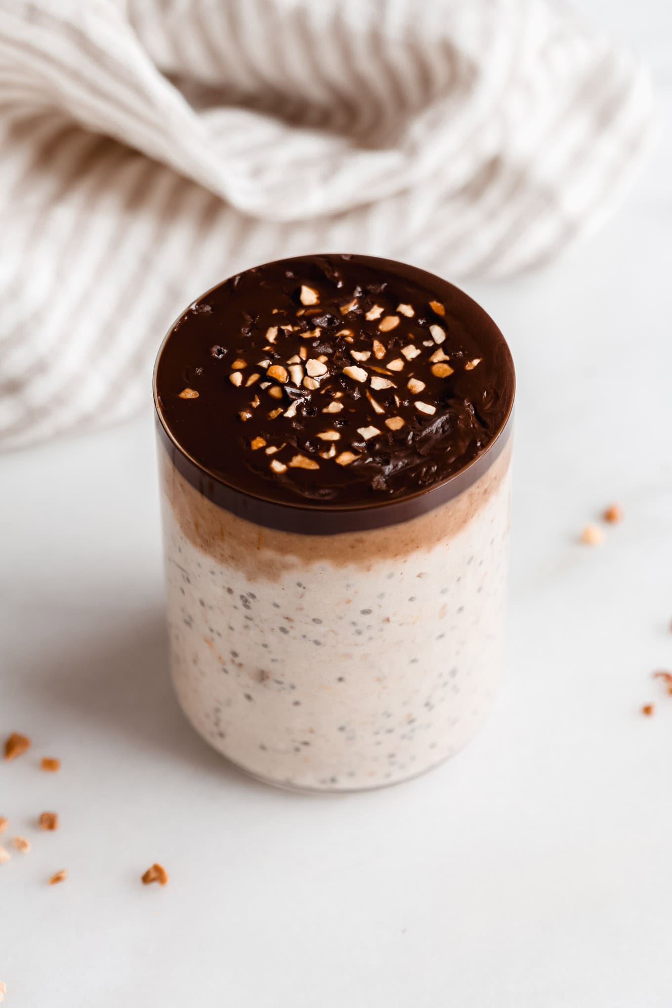 a cup of snickers overnight oats with a beige striped napkin in the back