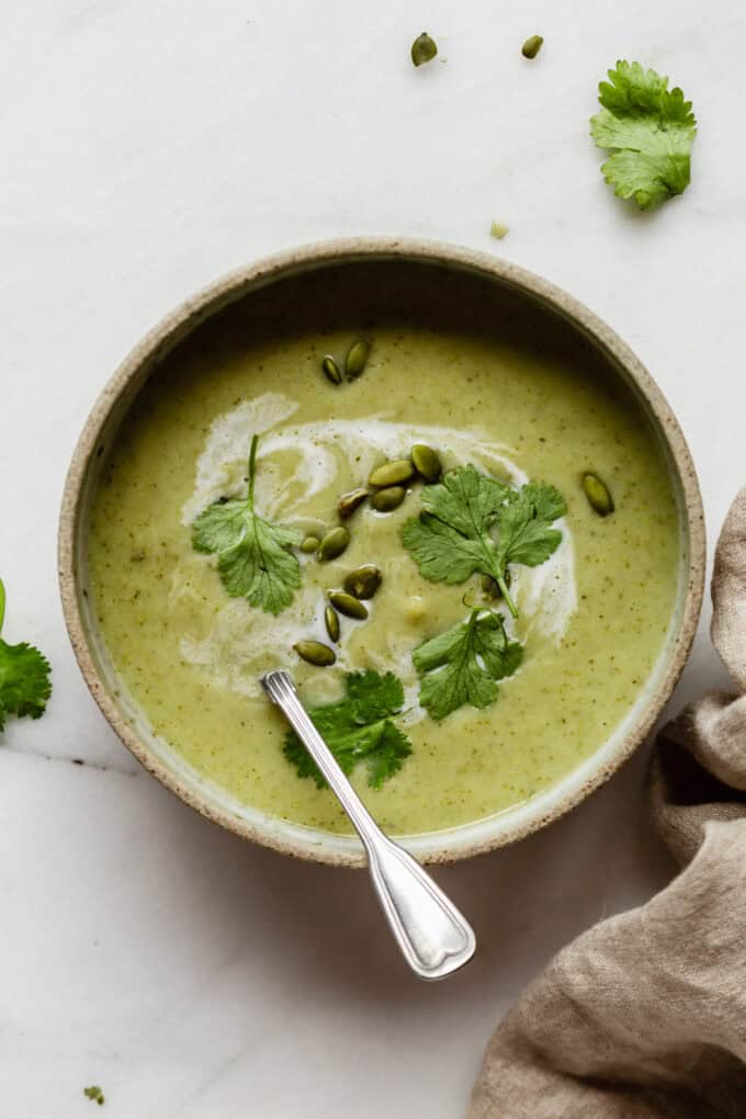 a bowl of broccoli cauliflower soup topped with cilantro and pumpkin seeds