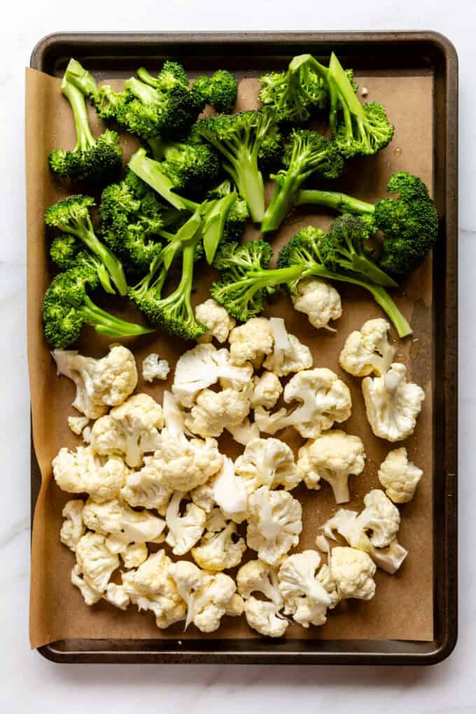 uncooked cut up broccoli and cauliflower on a baking sheet