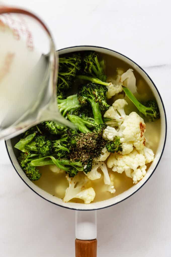 broth being poured into a pot of roasted broccoli and cauliflower