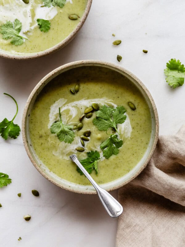 a bowl of broccoli cauliflower soup topped with cilantro and with a beige napkin on the side