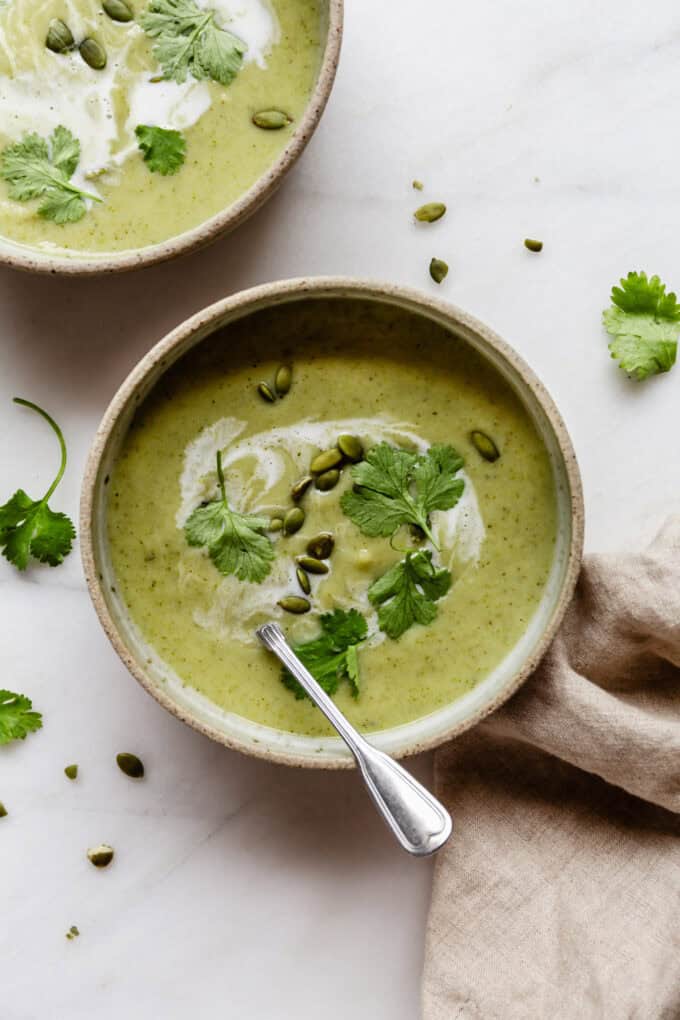 a bowl of broccoli cauliflower soup topped with cilantro and with a beige napkin on the side