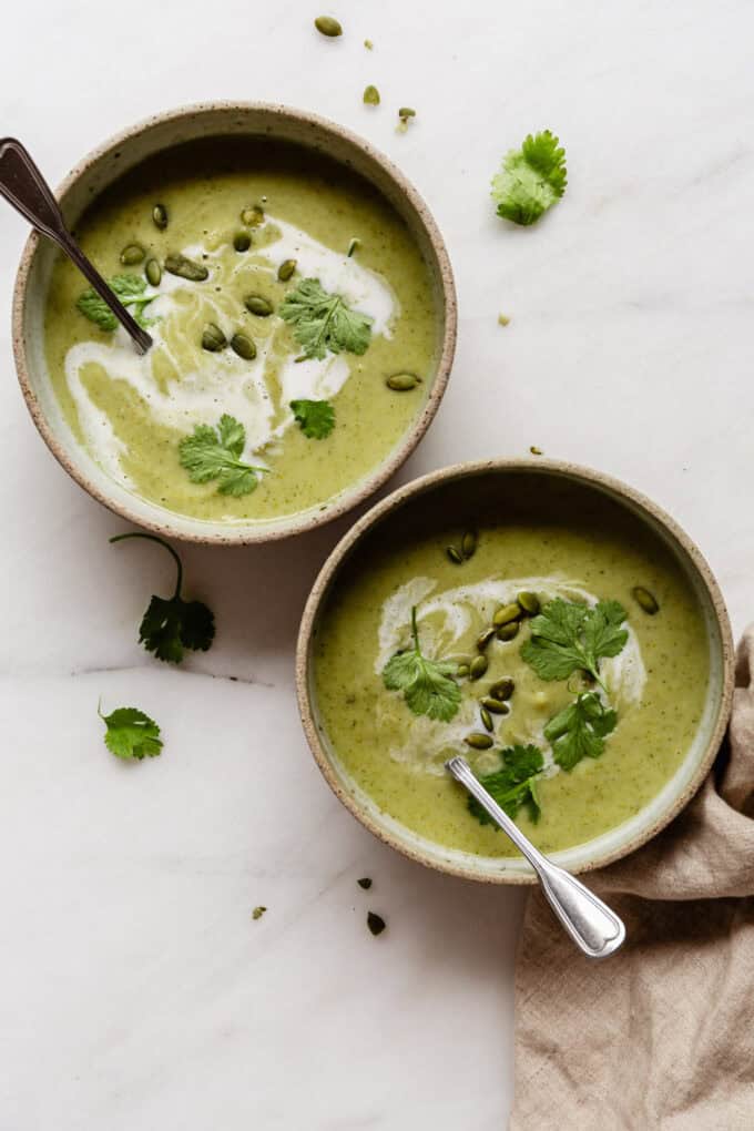 two bowls of broccoli and cauliflower soup with a beige napkin on the side