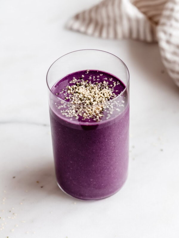 Berry protein smoothie in a tall glass with a stripped napkin on the side