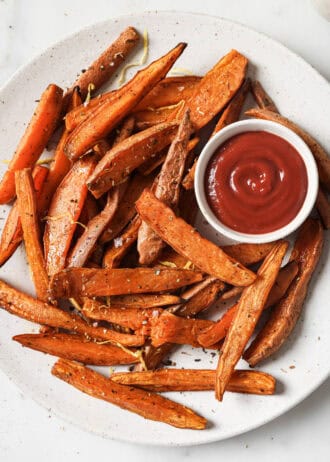 sweet potato wedges on a white plate with a side of ketchup