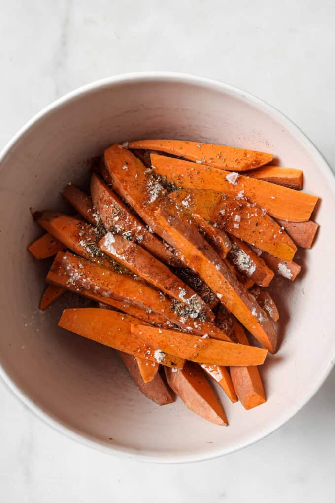 sweet potatoes cut into wedges with spices in a white mixing bowl