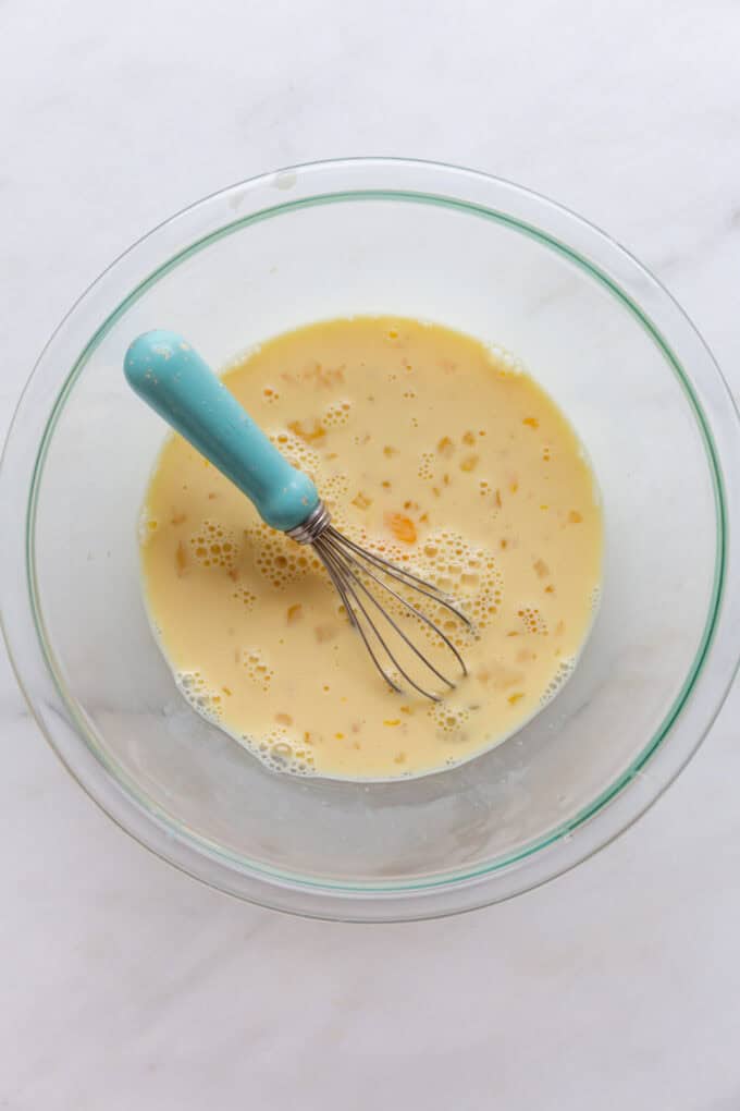 eggs and milk in a mixing bowl with a blue whisk