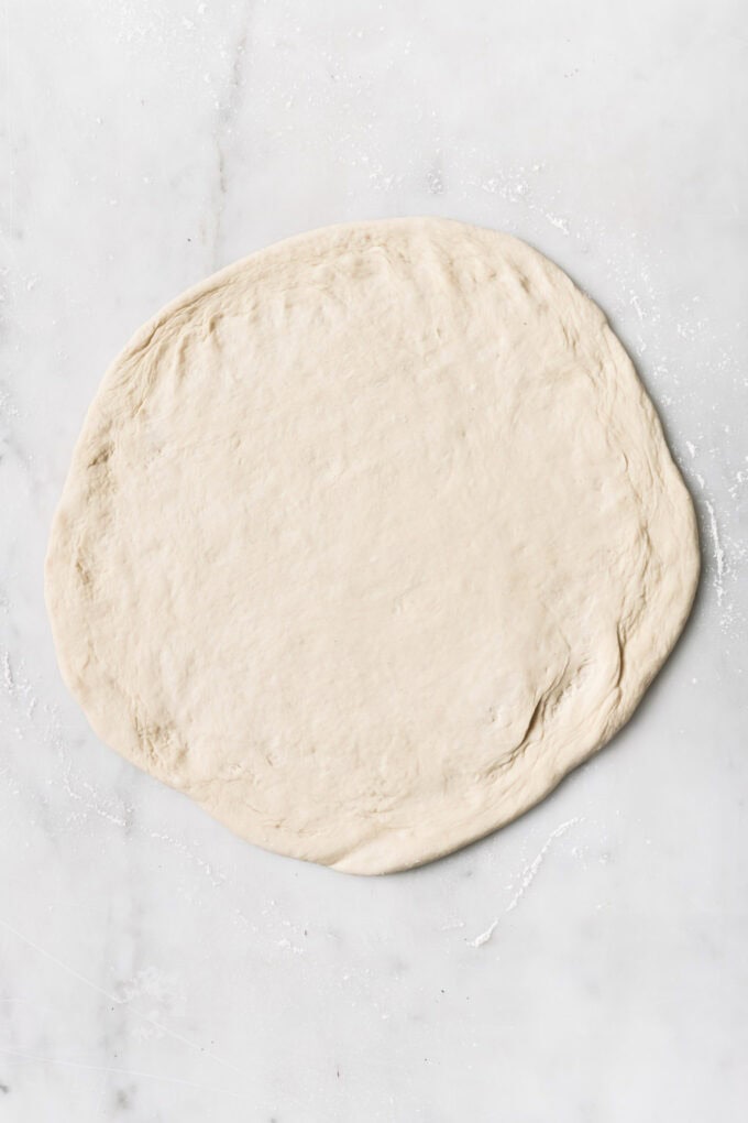 rolled out pizza dough on a marble counter