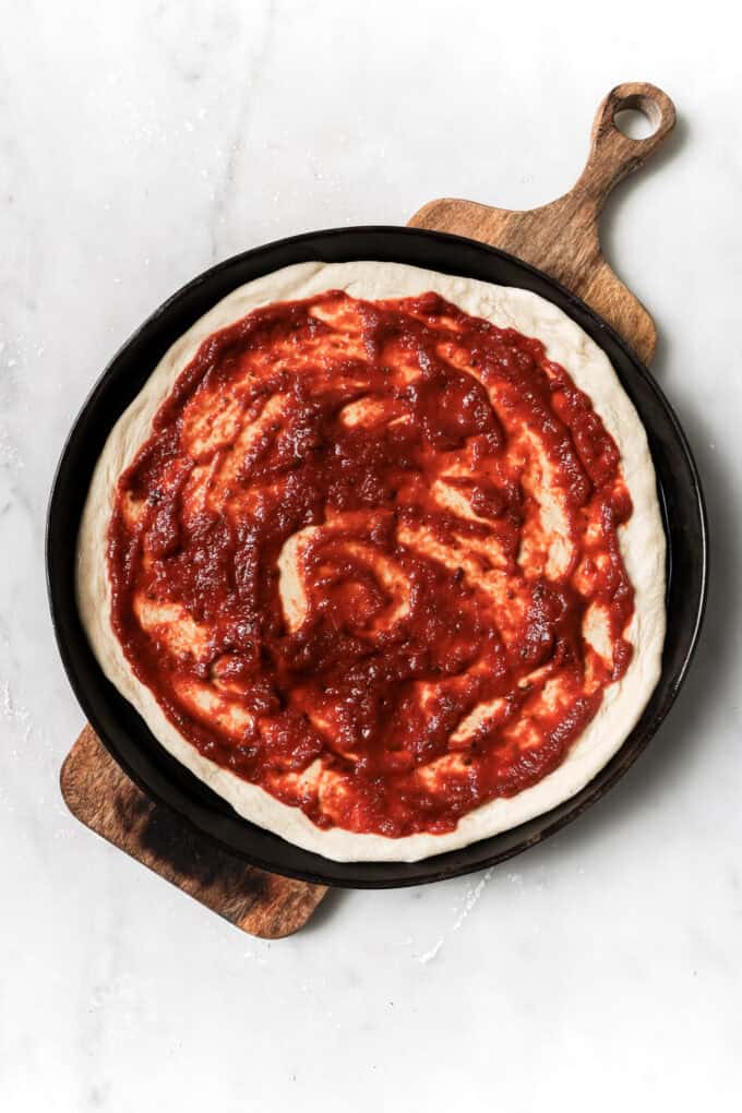 pizza dough topped with pizza sauce on a wood board