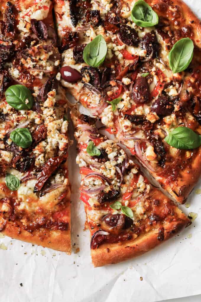 sliced mediterranean pizza topped with fresh basil leaves