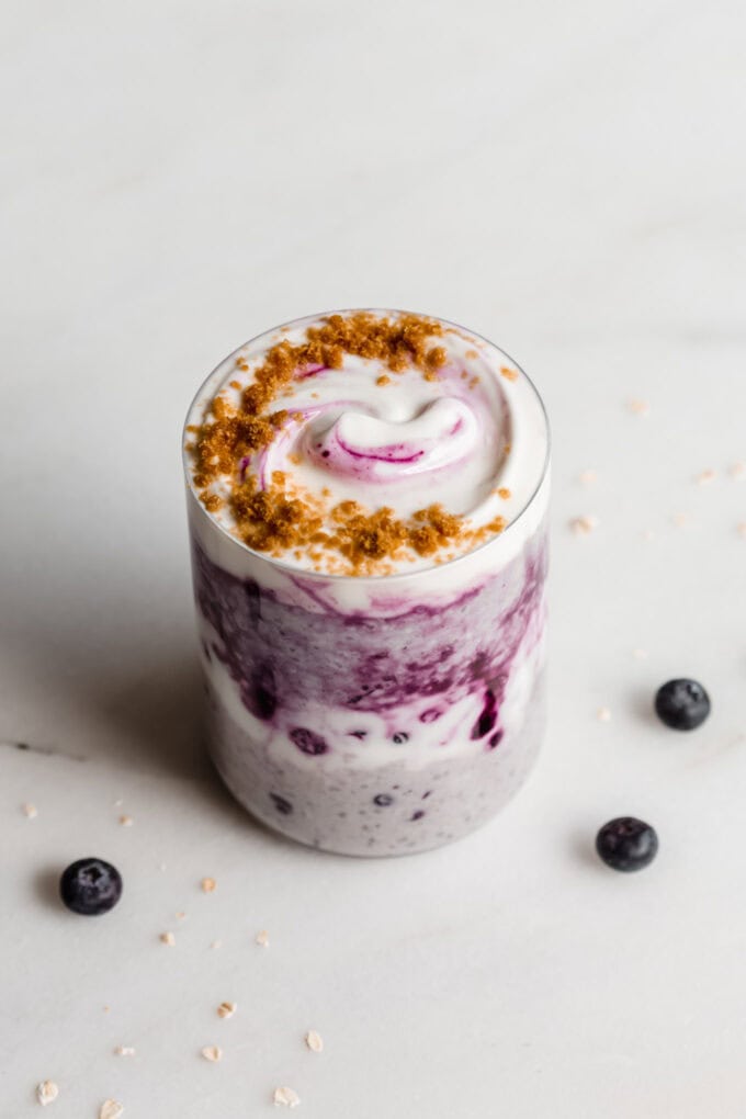 Blueberry overnight oats in a jar on a white marble counter with blueberries around it.