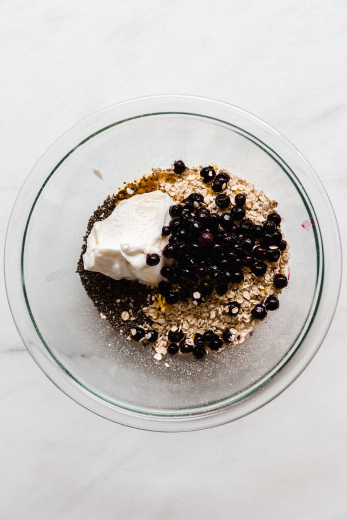 oats, yogurt, chia seeds and blueberries in a clear mixing bowl.